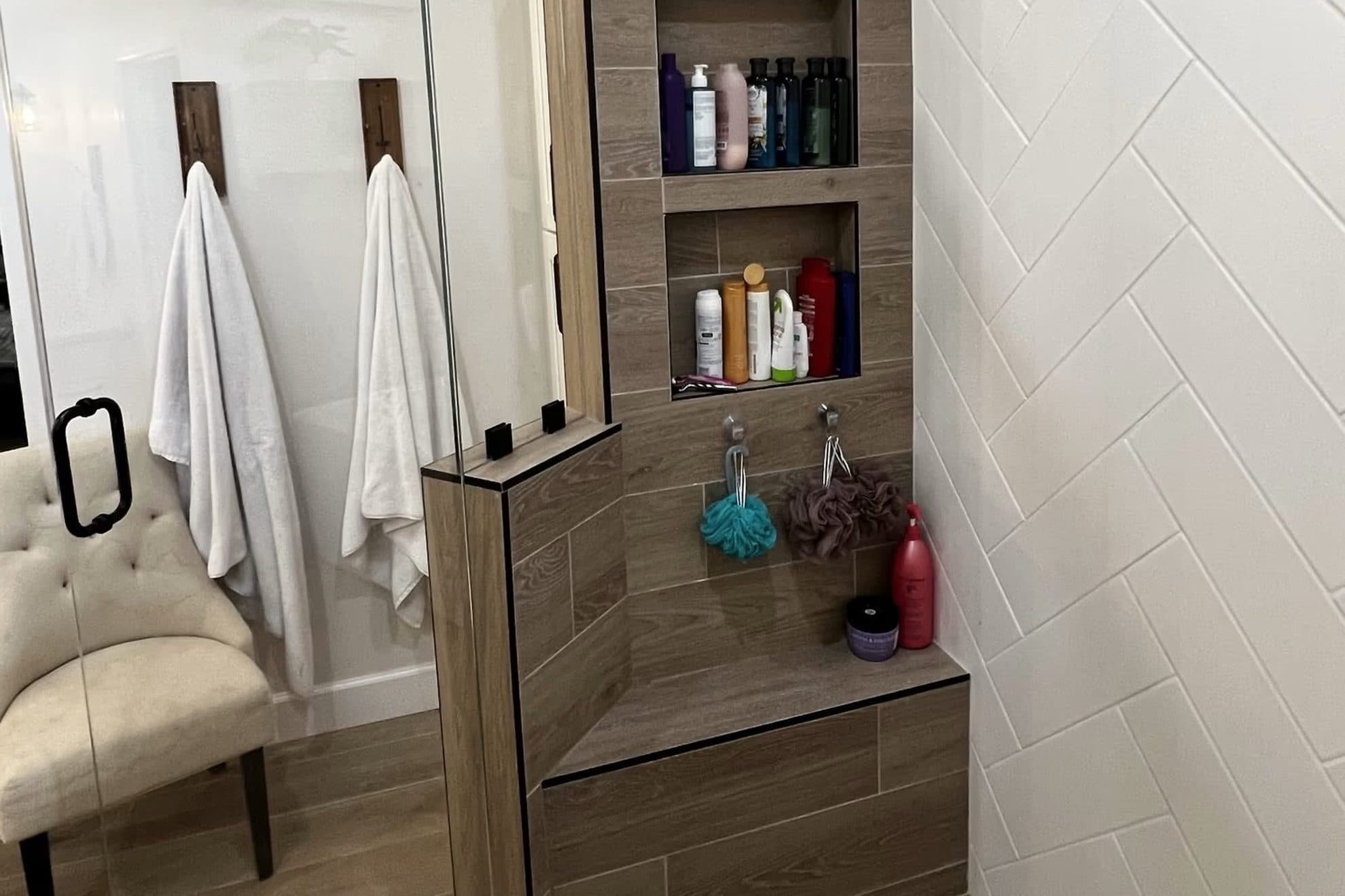 Tiled walk-in shower with a built-in bench seat and two recessed niches, beside a glass door and towel hooks
