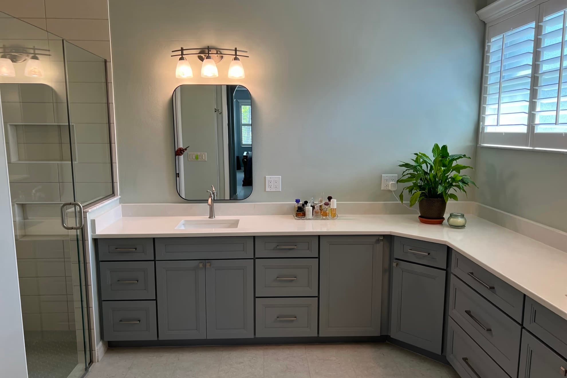 Remodeled bathroom with a gray vanity, a white countertop, a glass shower enclosure on the left, and a large light tile floor