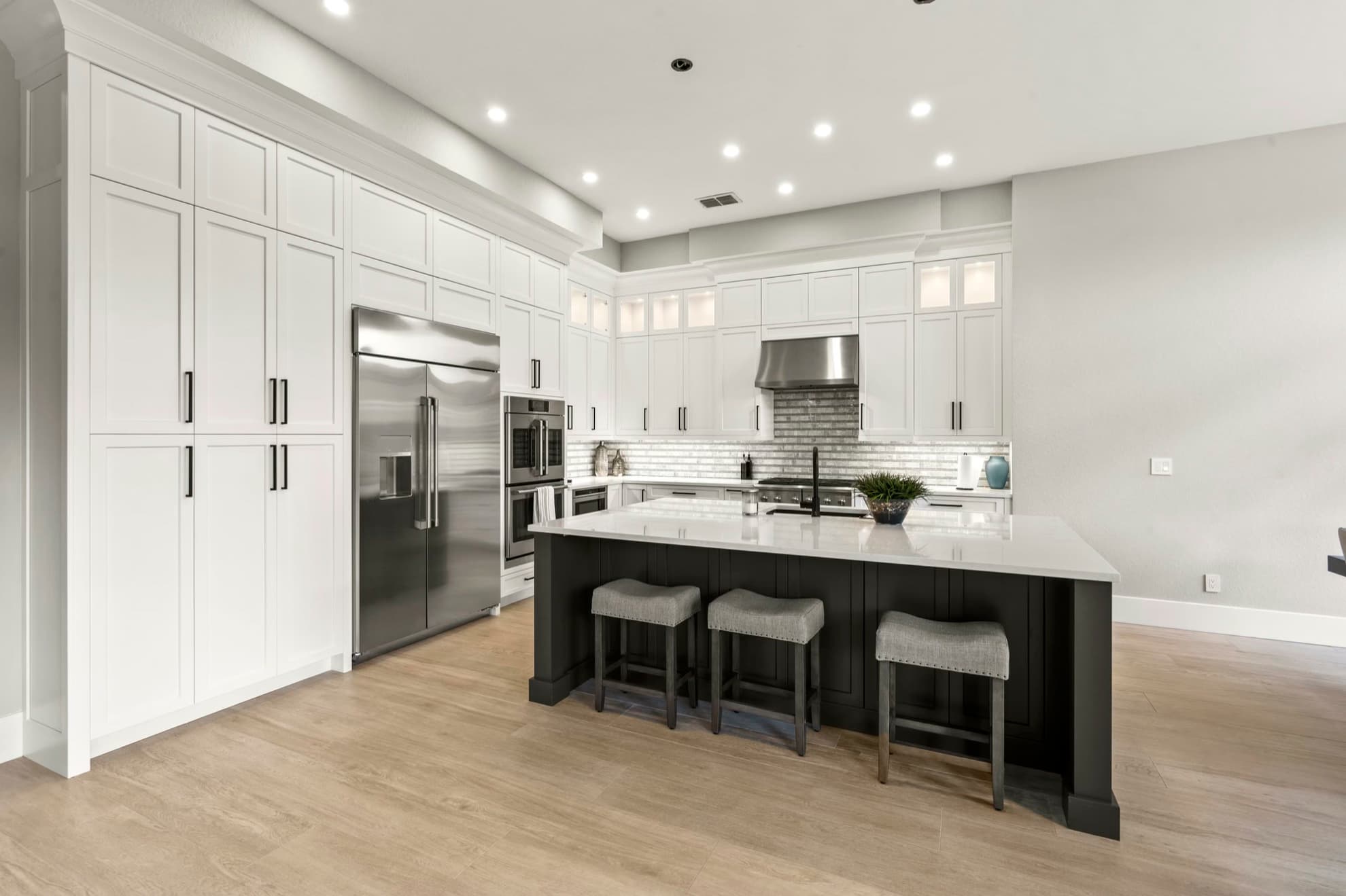 Kitchen with white shaker cabinets running to the ceiling, a dark island with counter stools, and light wood look flooring
