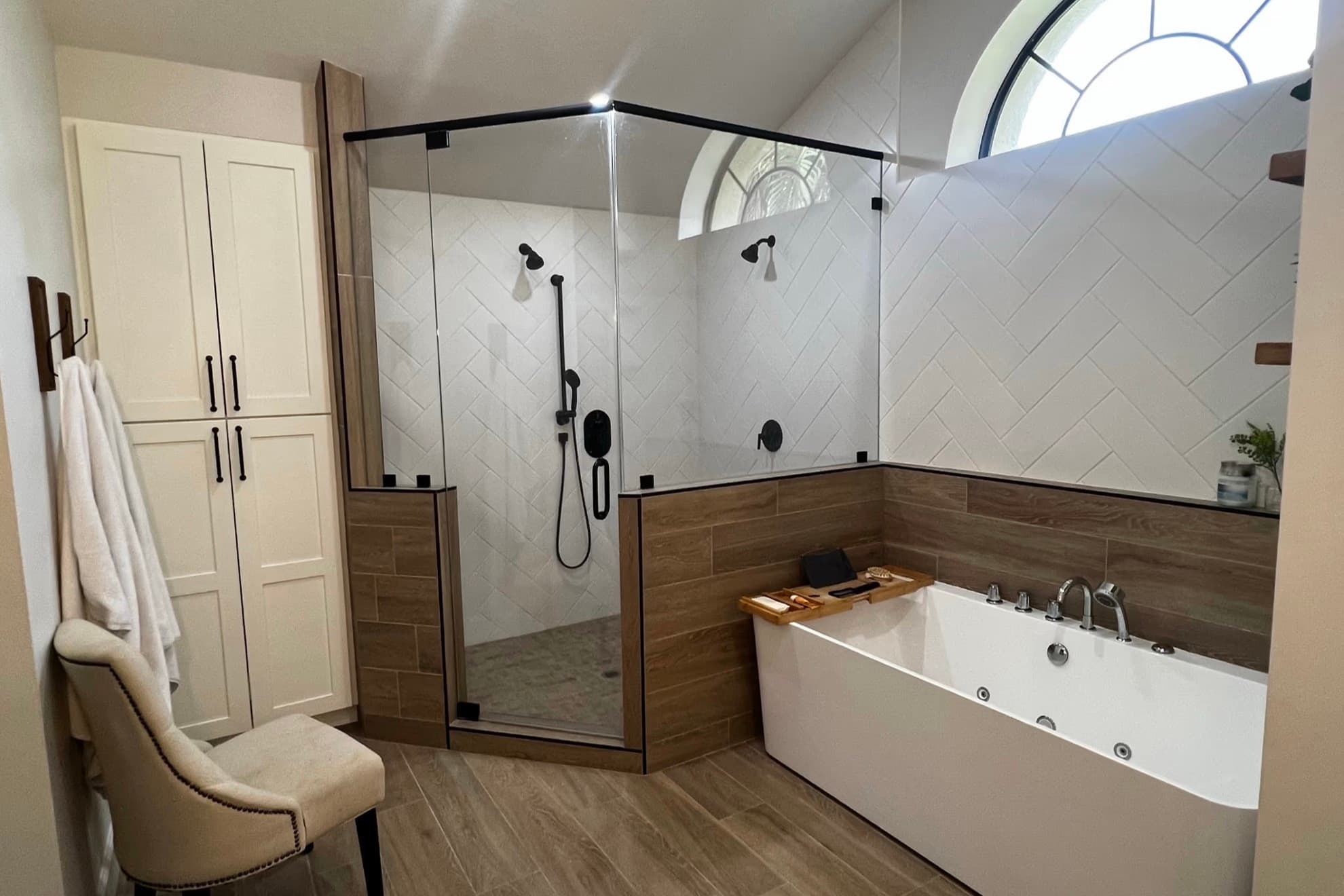 Corner glass shower enclosure with a low threshold, handheld shower on a slide bar and herringbone wall tile, next to a freestanding soaking tub in a remodeled bathroom