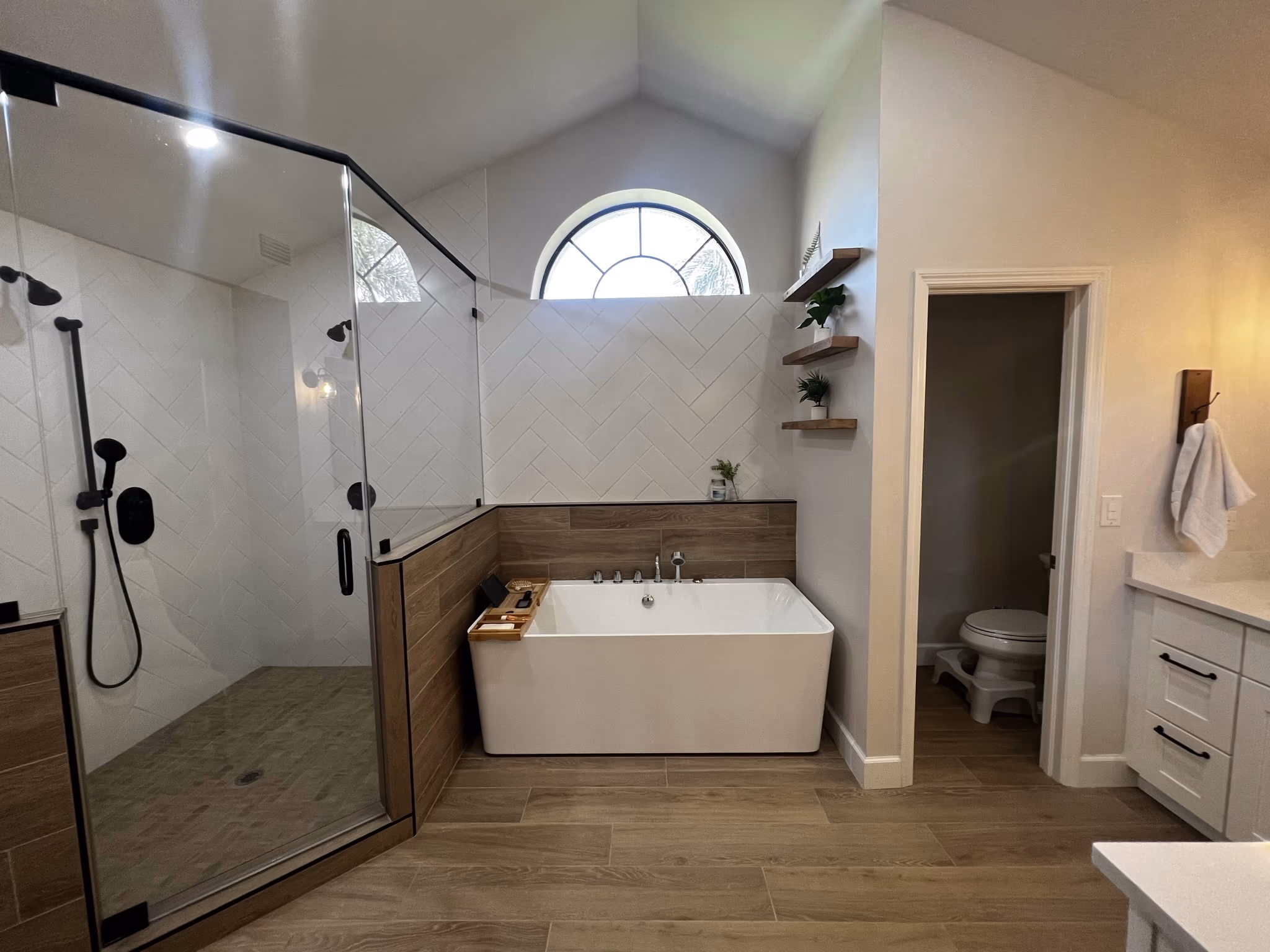 Bathroom with a glass corner shower, freestanding tub beneath an arched window, and a doorway to a separate toilet room