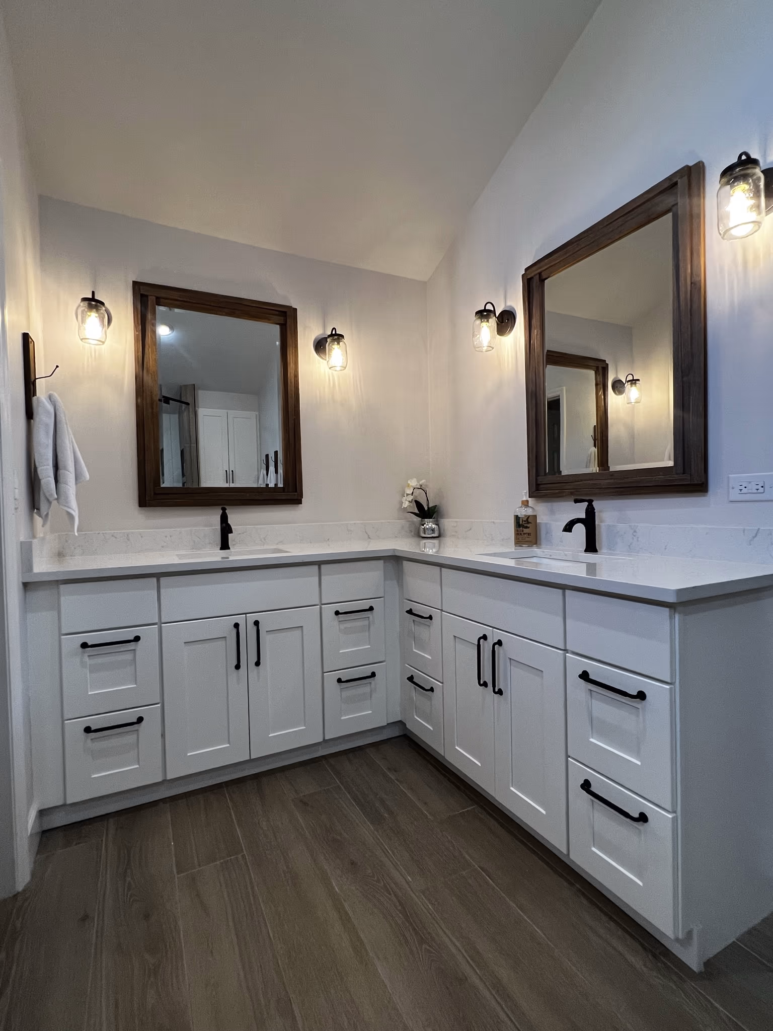Double vanity with white shaker cabinets, two dark wood-framed mirrors, and mason jar wall sconces