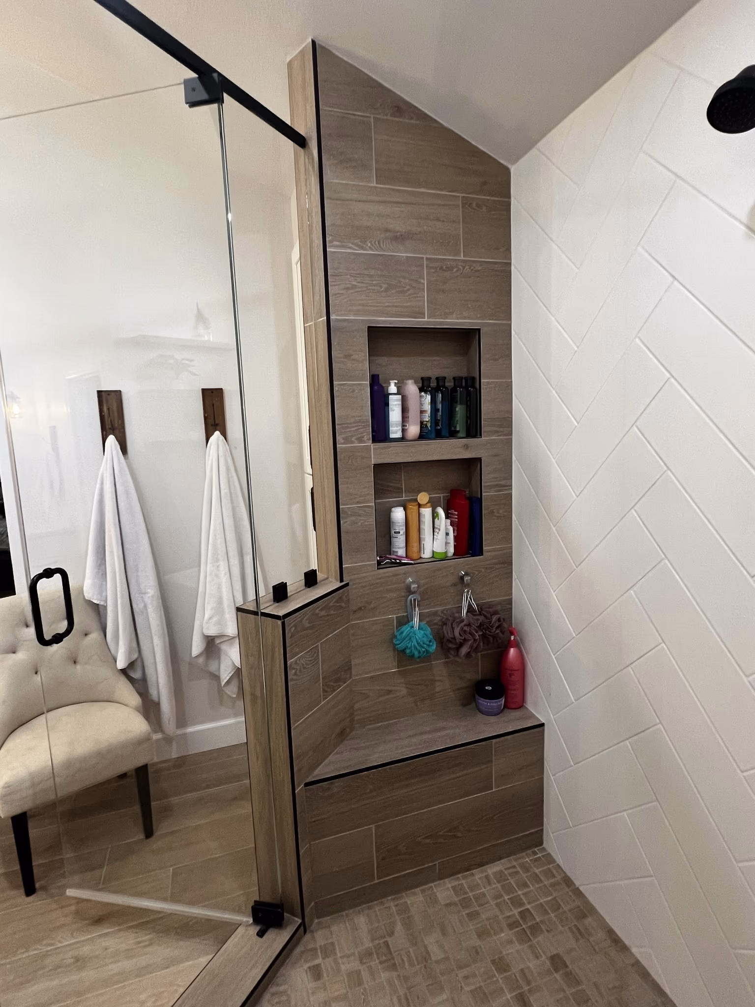 Shower niche with two tiled shelves holding bottles, above a built-in bench seat in the wood-tile shower wall