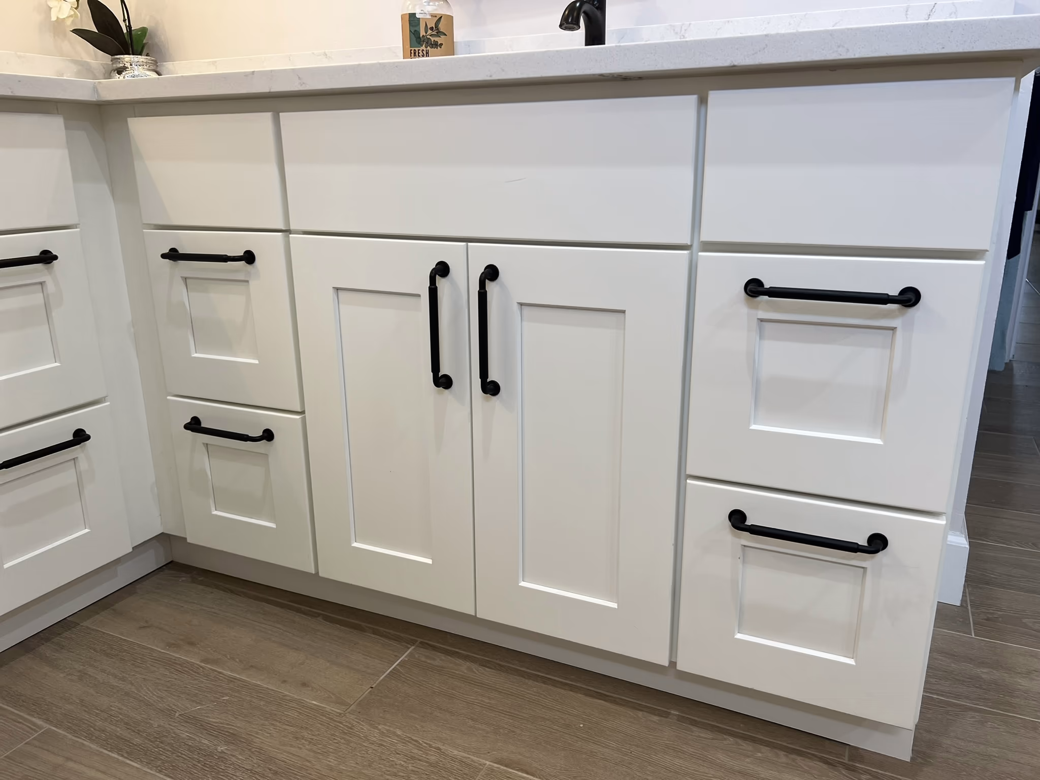 Close-up of white shaker vanity cabinets with black bar pulls beneath a white quartz countertop