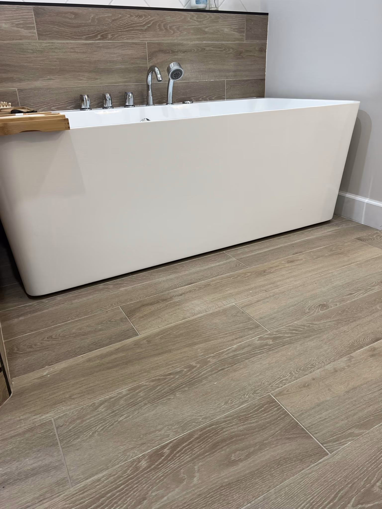 Close-up of the freestanding tub base and chrome fixtures on the wood-look tile floor