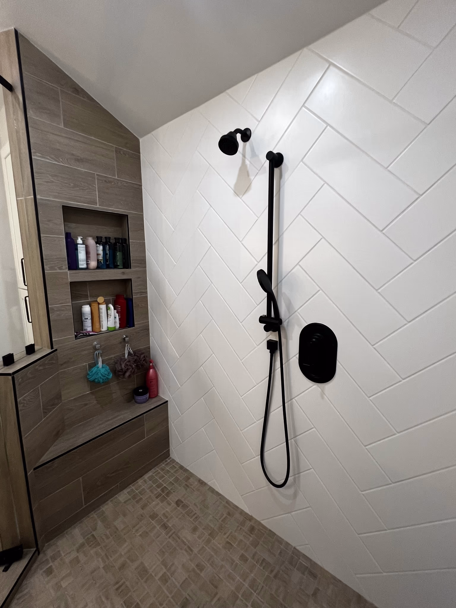 Single black shower head and handheld sprayer on a slide bar against herringbone-patterned tile