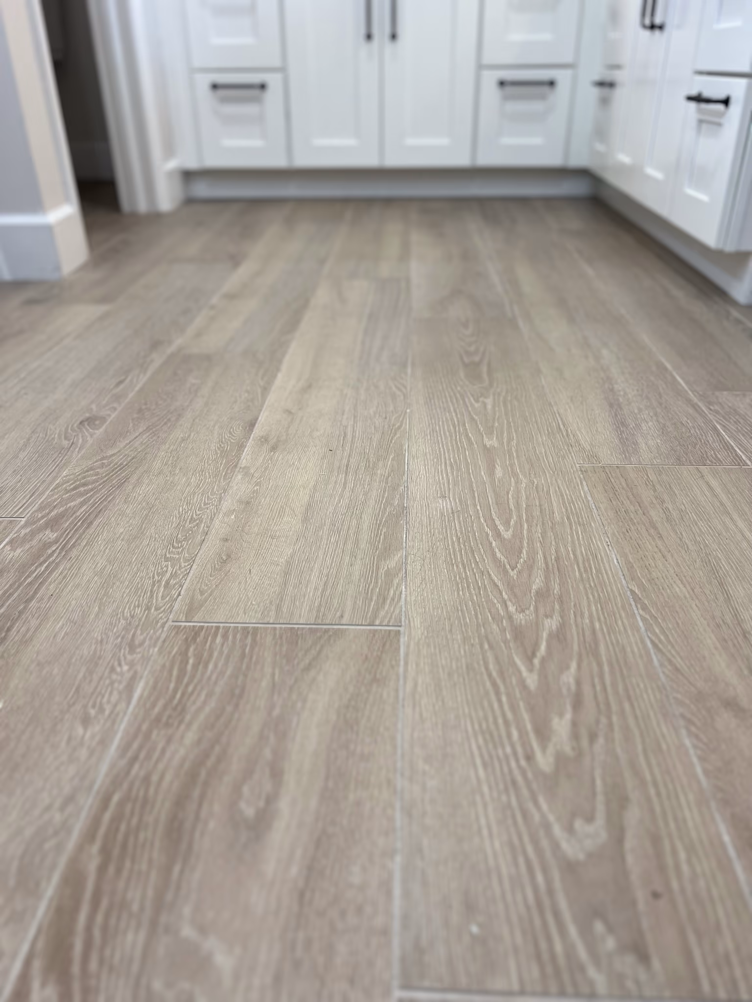 Wood-look tile flooring shown at a low angle, leading toward the white vanity cabinets