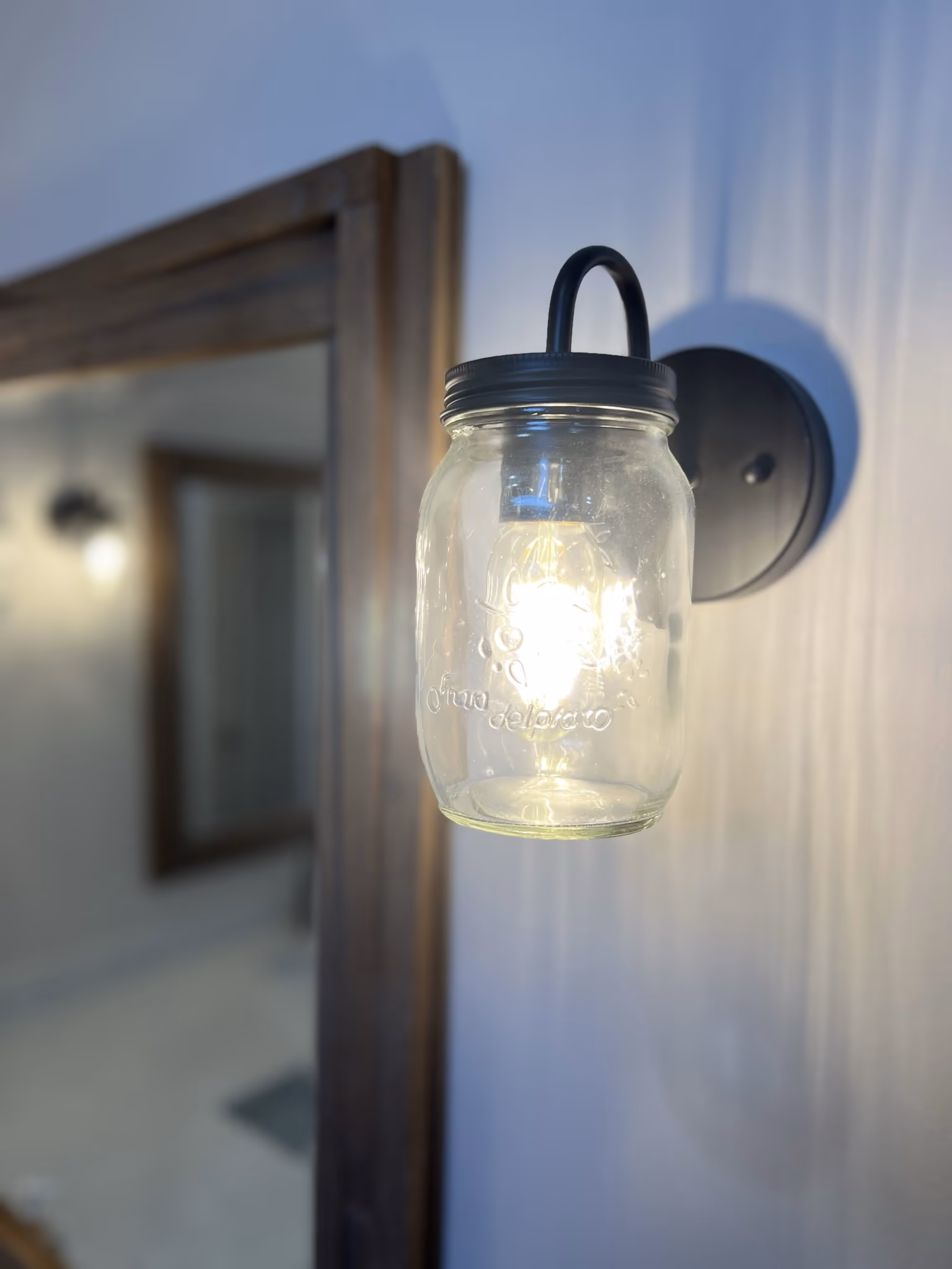 Close-up of a mason jar wall sconce beside a dark wood-framed mirror