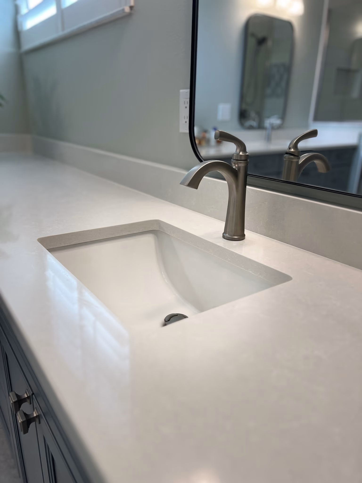Close-up of an undermount sink with a brushed nickel faucet set into a white quartz vanity counter