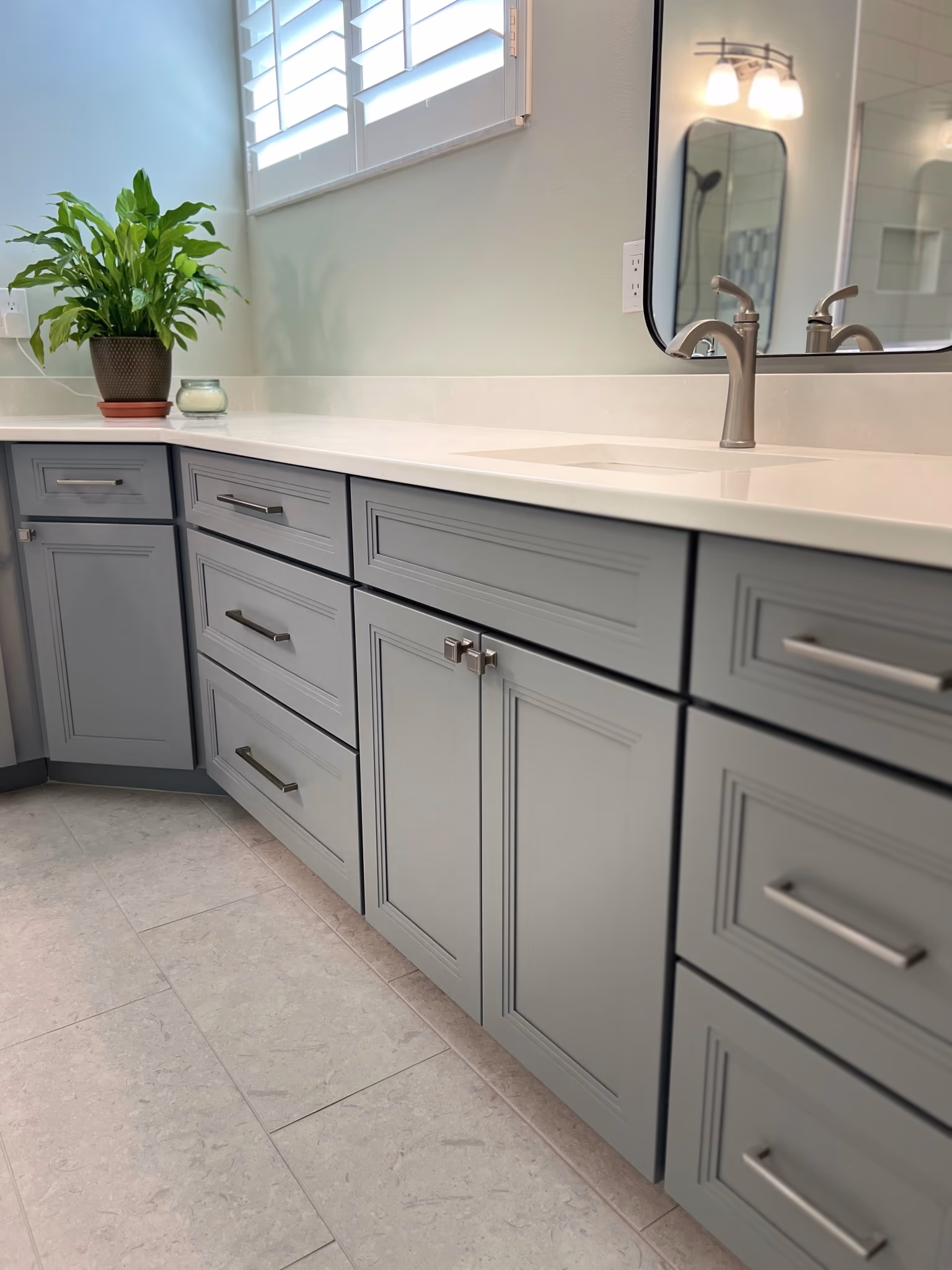 Vanity counter with a potted plant and faucet, mirror reflecting the shower, above grey shaker cabinets