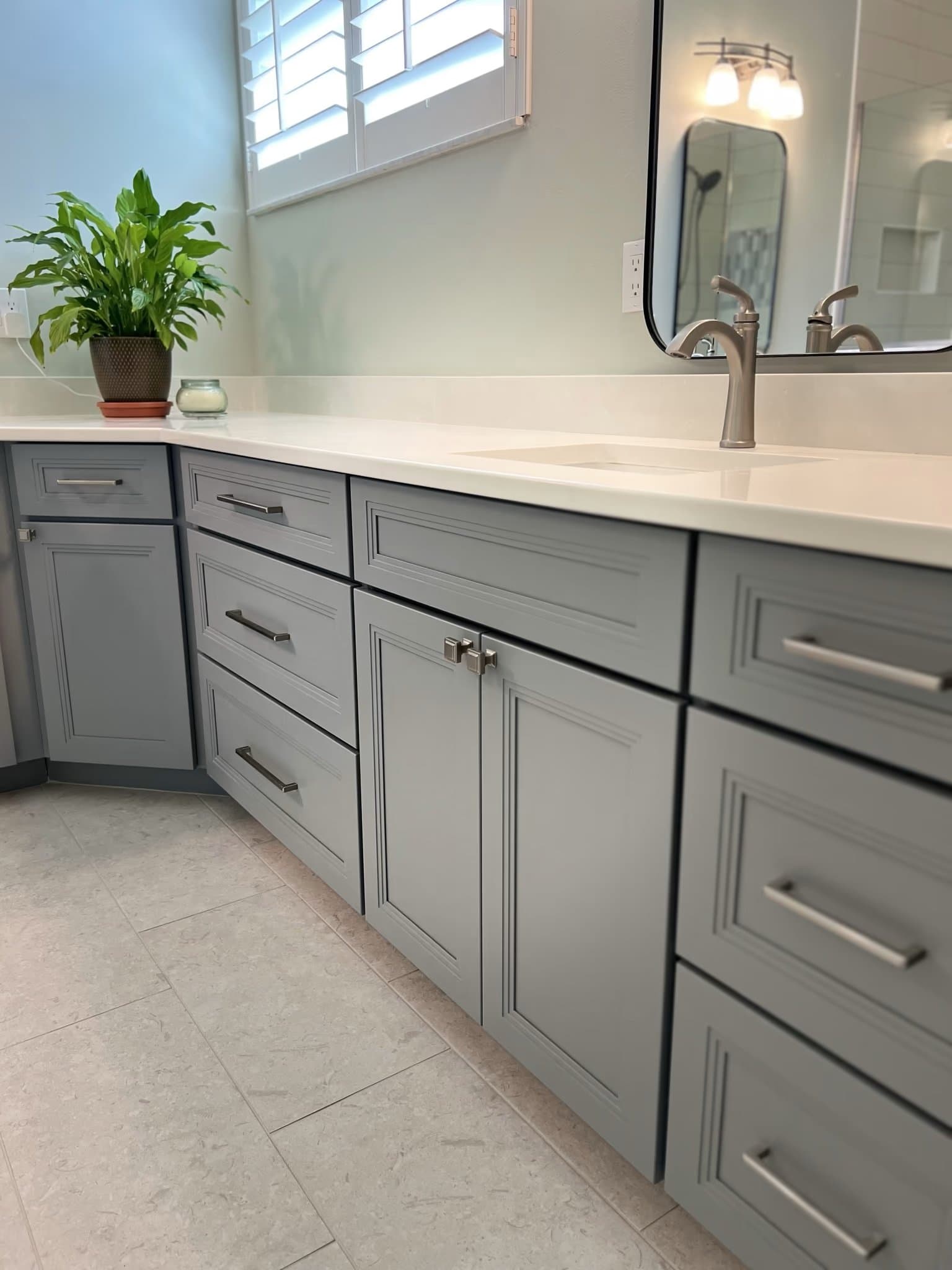 Vanity counter with a potted plant and faucet, mirror reflecting the shower, above grey shaker cabinets