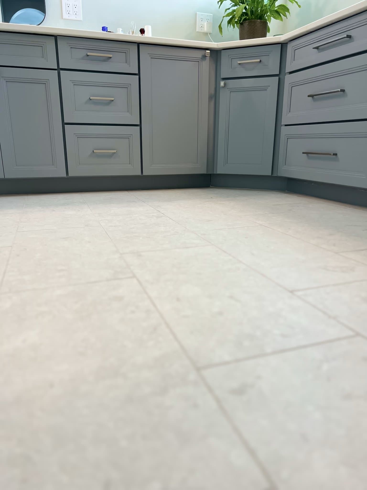 Grey tile flooring meeting a grey shaker cabinet corner, with a potted plant on the counter above