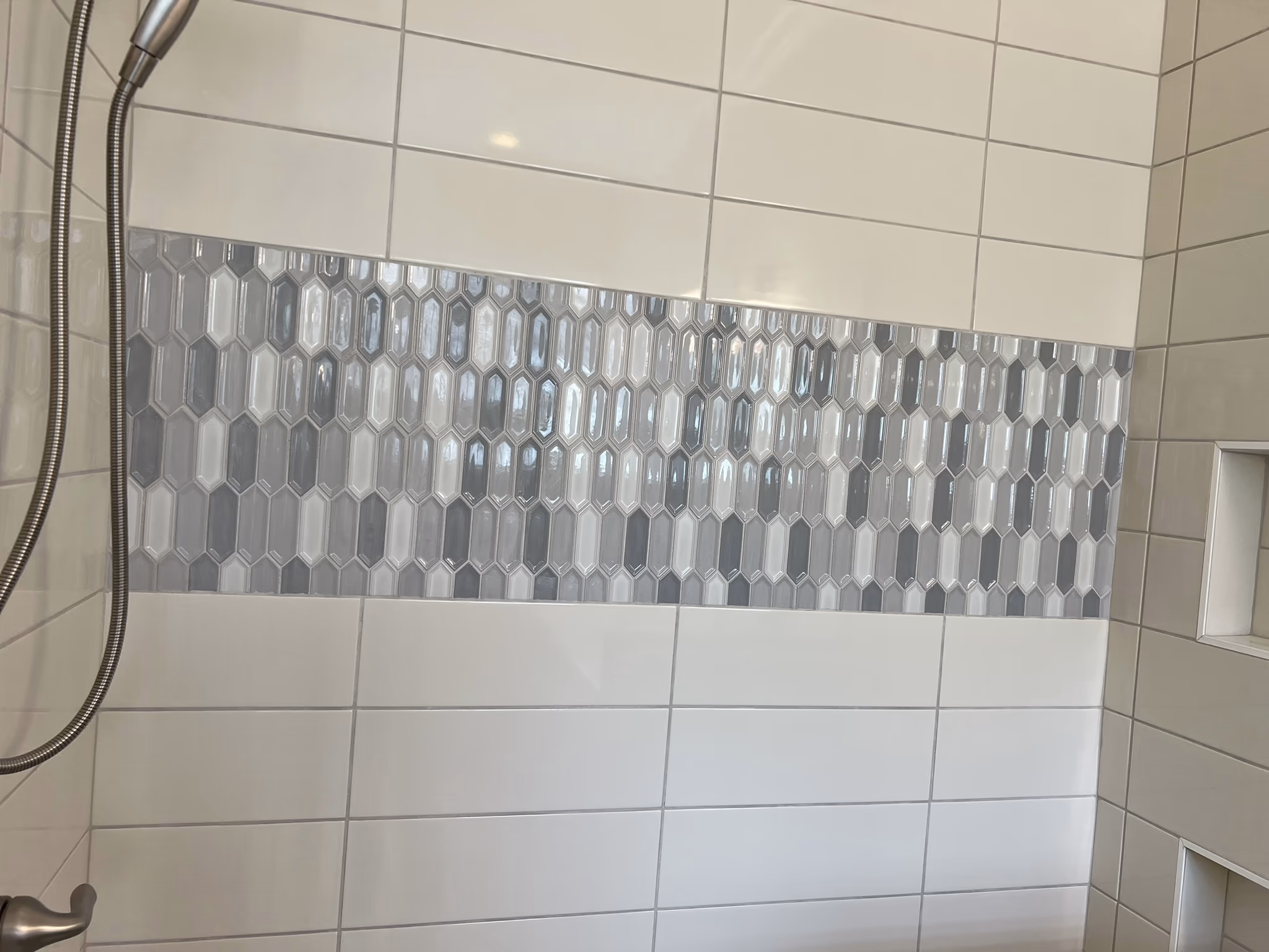 Shower wall with white subway tile and a horizontal band of grey and white elongated hexagon mosaic tile