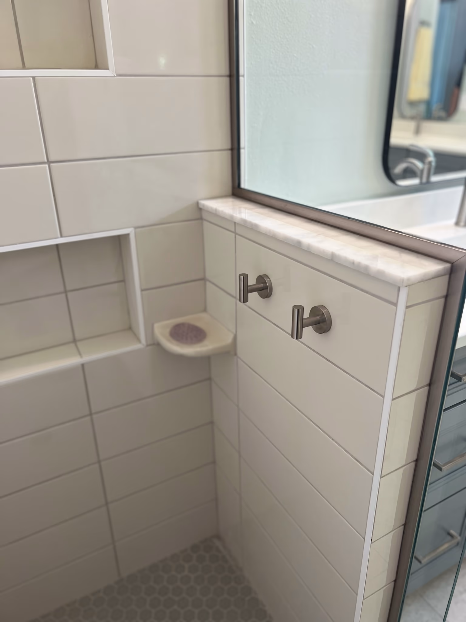 Corner of a shower with a tiled niche, marble ledge, soap dish, and two towel hooks