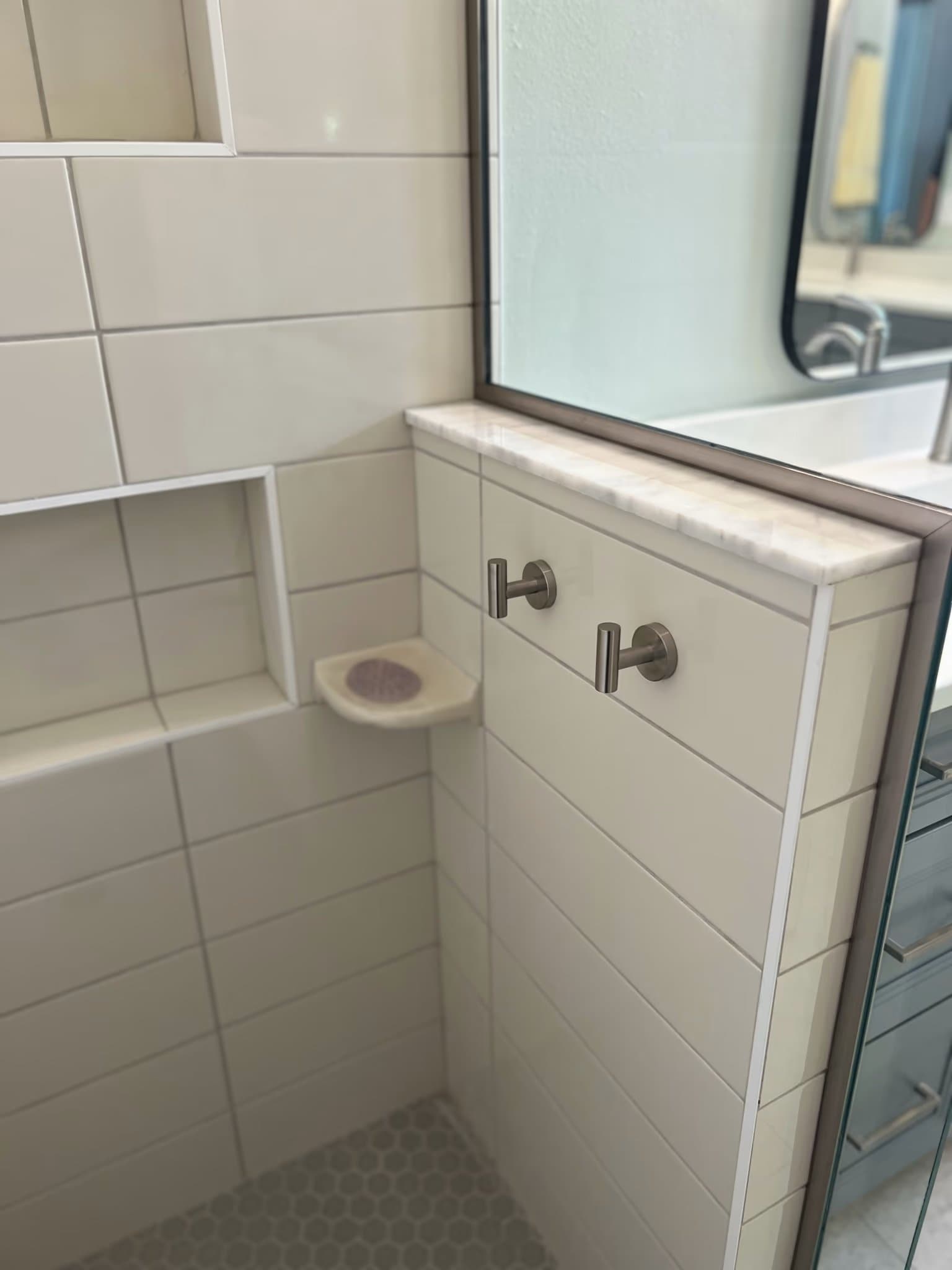 Corner of a shower with a tiled niche, marble ledge, soap dish, and two towel hooks