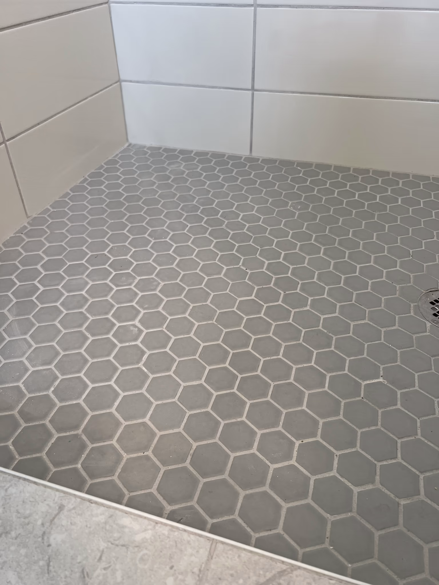 Grey hexagon mosaic tile shower floor with a drain, bordered by white subway tile walls