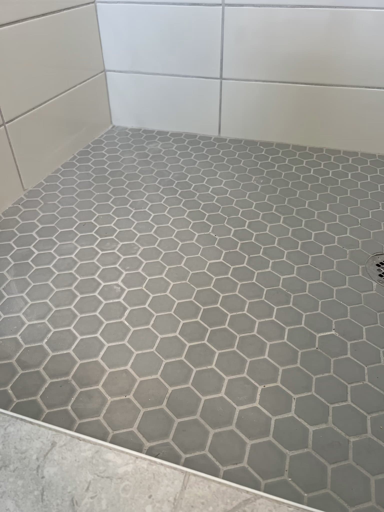 Grey hexagon mosaic tile shower floor with a drain, bordered by white subway tile walls