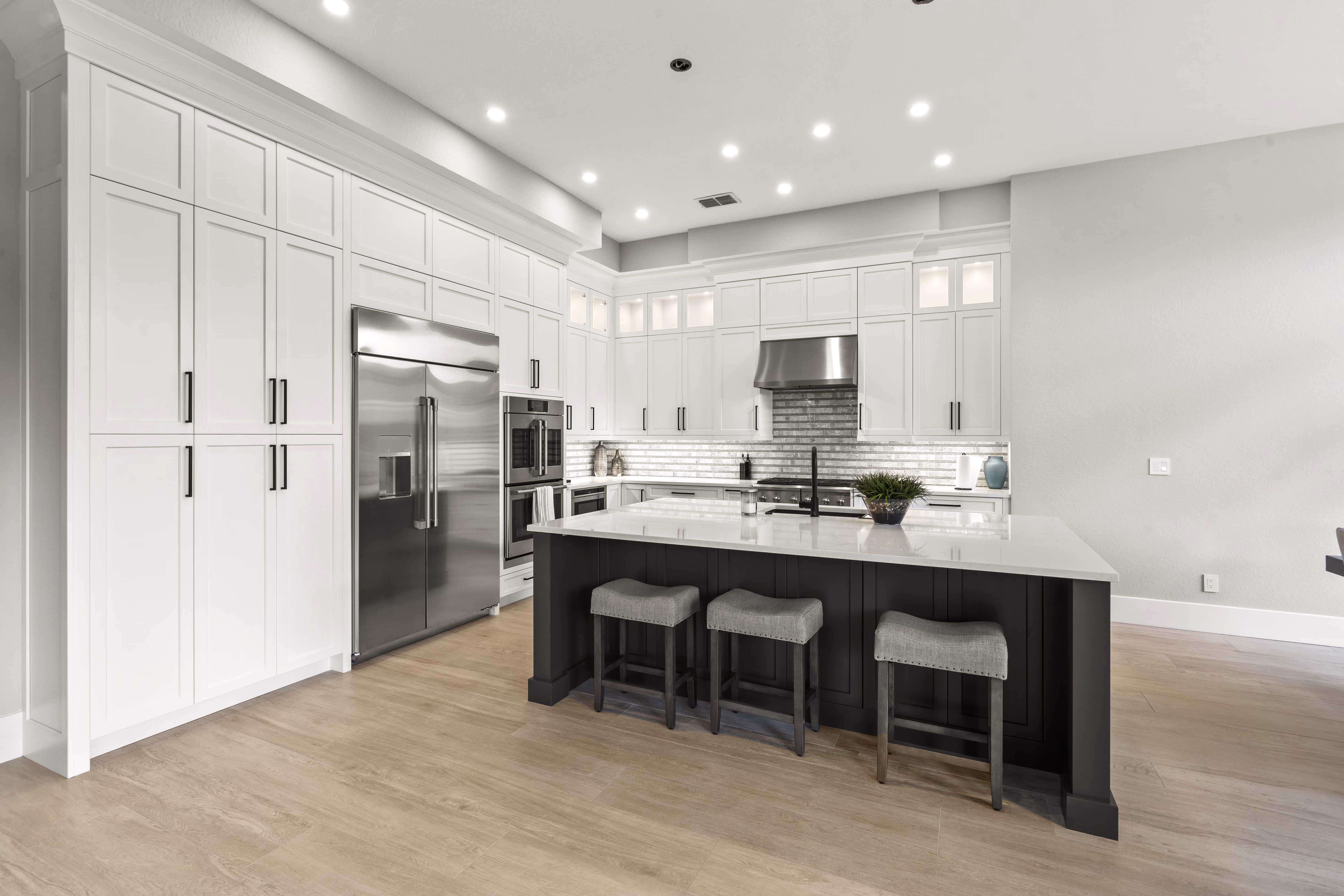 Kitchen with white floor-to-ceiling cabinetry, a stainless refrigerator, and a dark island with quartz counter