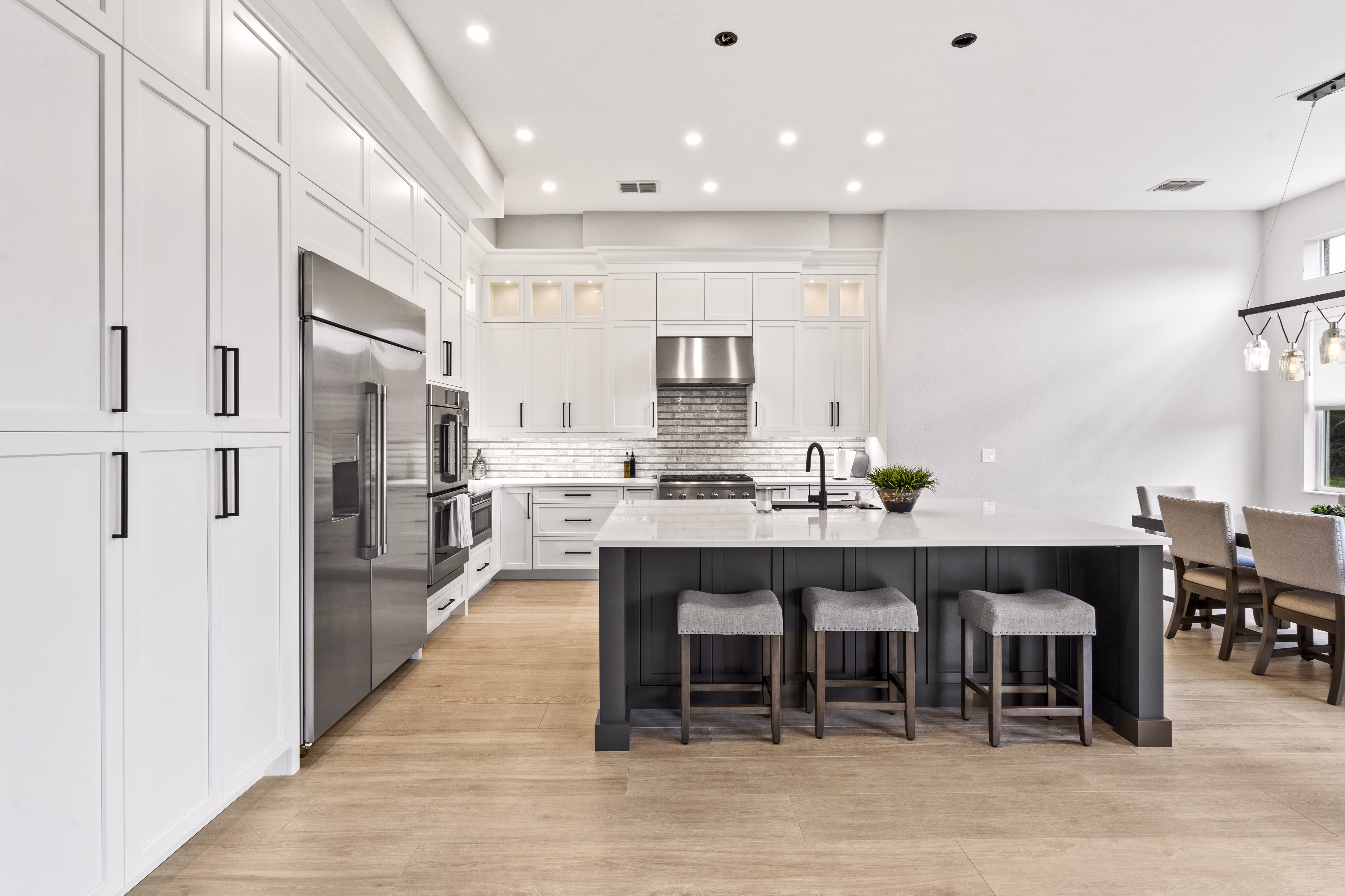 Kitchen island with quartz counter and three grey stools, opening to a dining area with pendant lighting in the background
