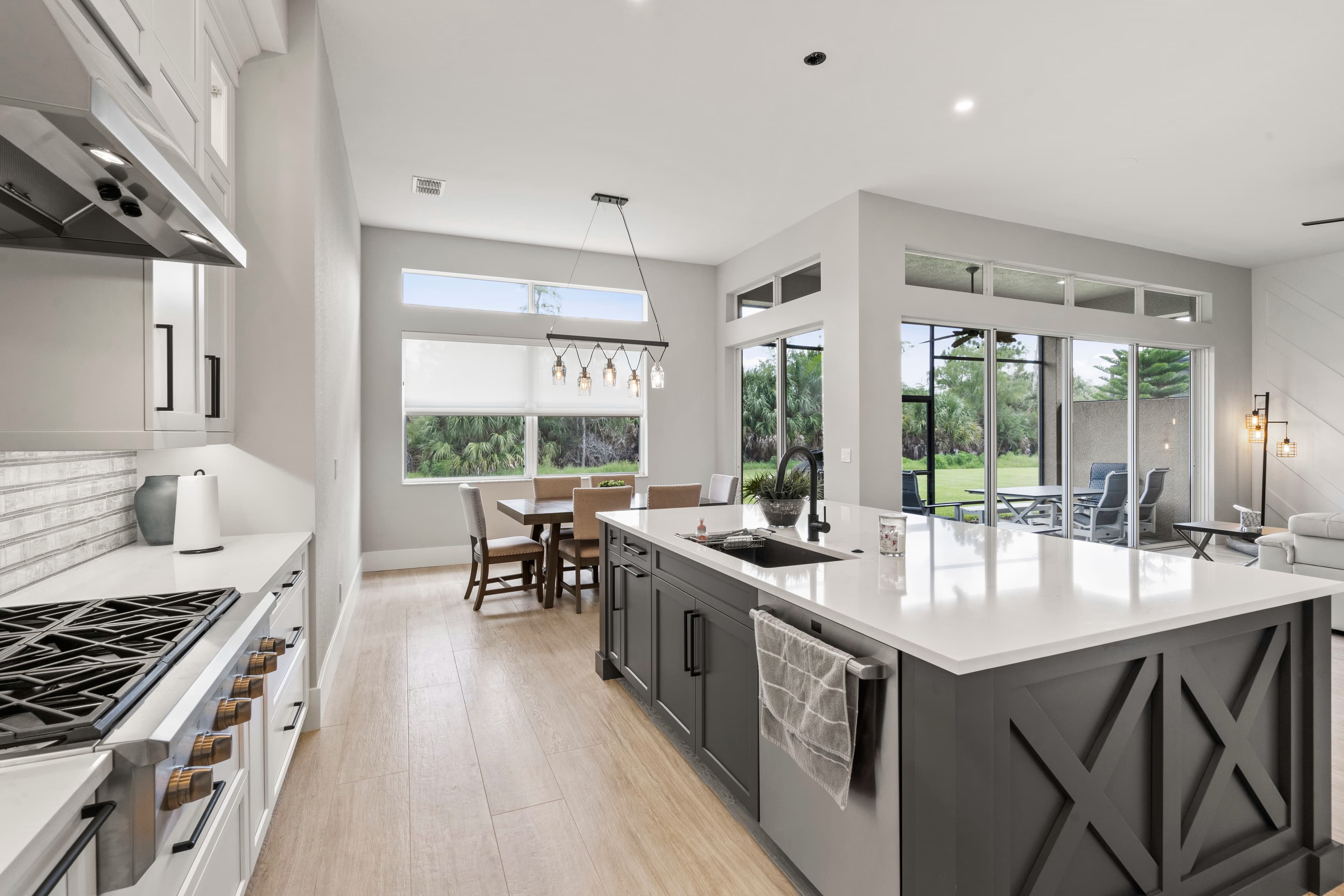 Kitchen island with dark X-pattern cabinet doors and a black gooseneck faucet, gas range beyond with sliding doors to a lanai