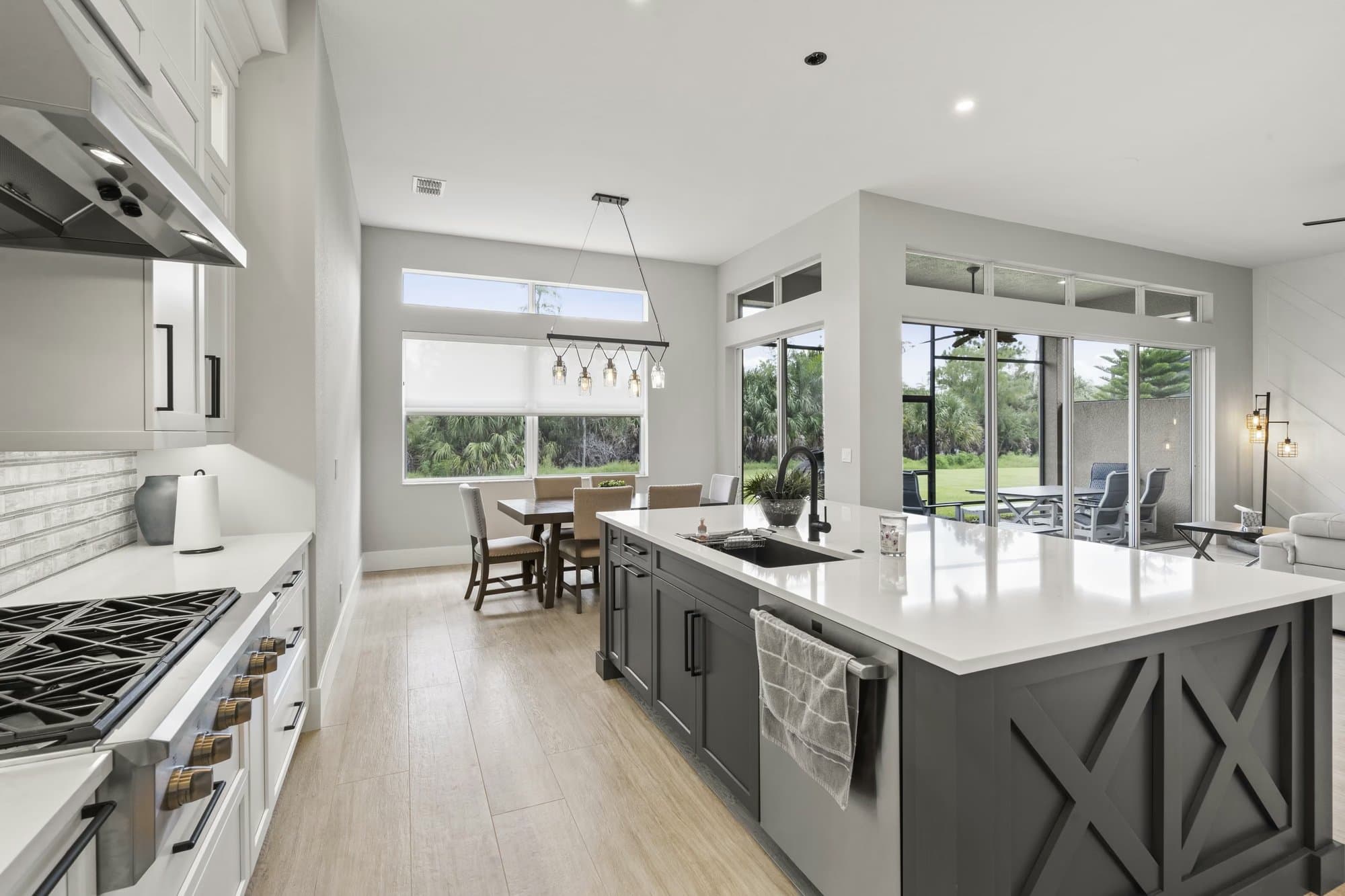 Kitchen island with dark X-pattern cabinet doors and a black gooseneck faucet, gas range beyond with sliding doors to a lanai