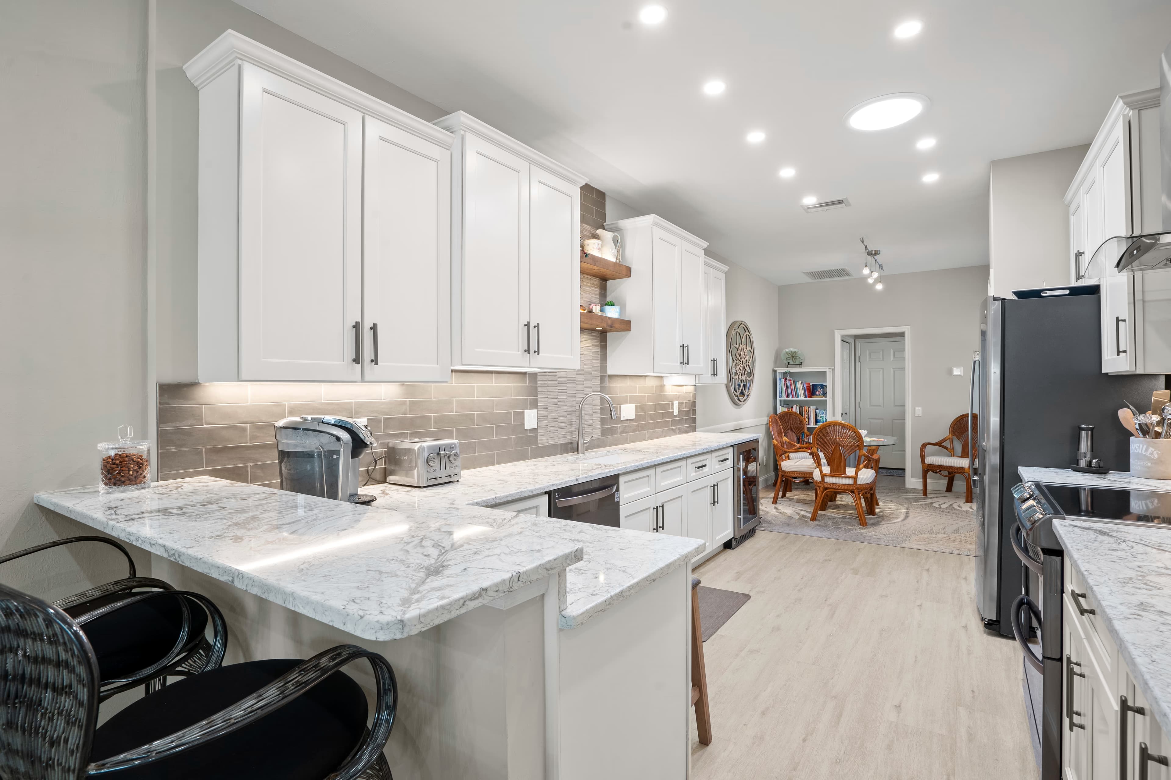 Kitchen peninsula with a waterfall-edge quartz counter and a black dishwasher below, opening to a sitting area
