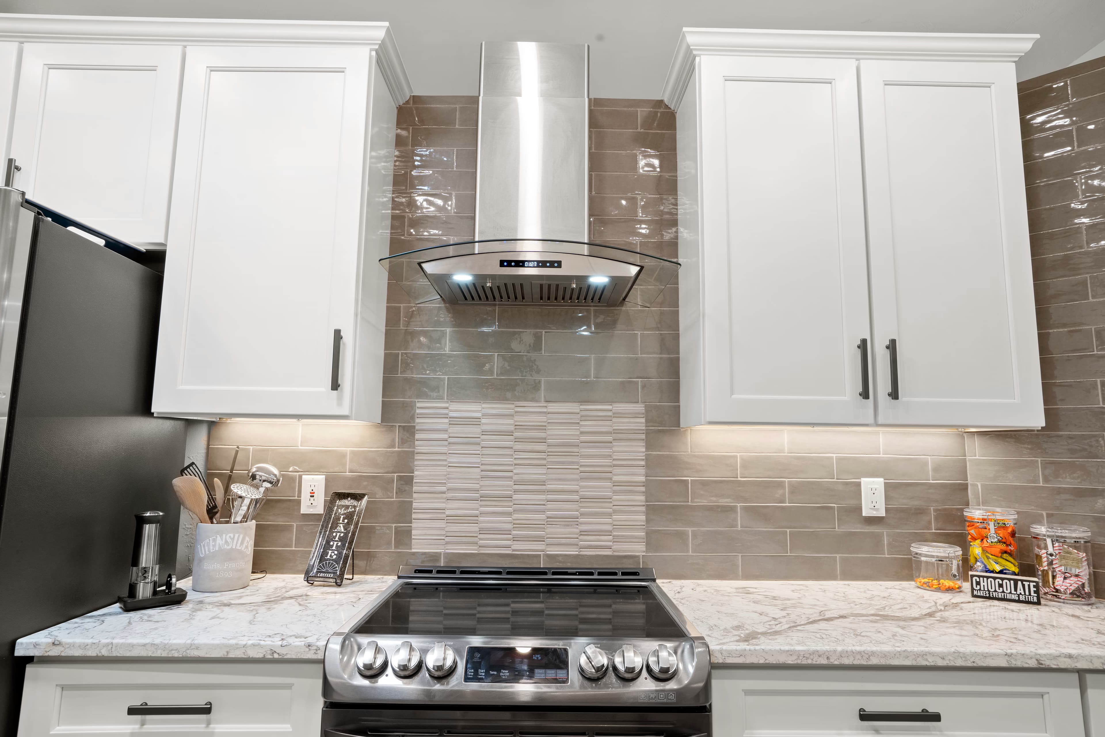 Close-up of a curved glass range hood above a black range with a mosaic tile backsplash accent
