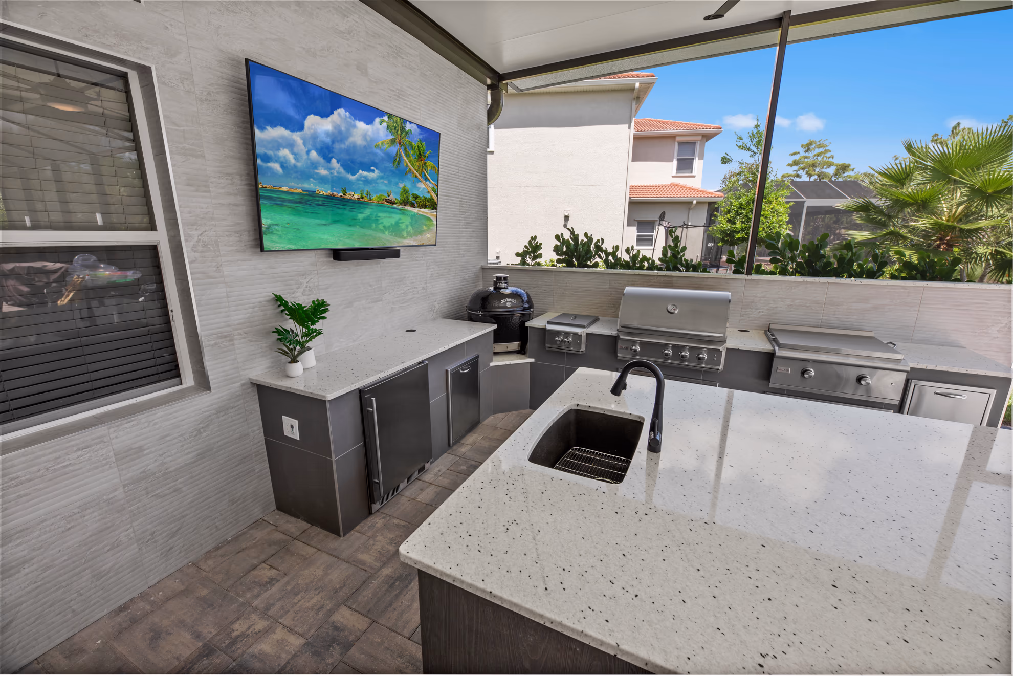 Close view of the outdoor kitchen counter with a potted plant, mini fridge, and kamado grill beneath a wall-mounted TV