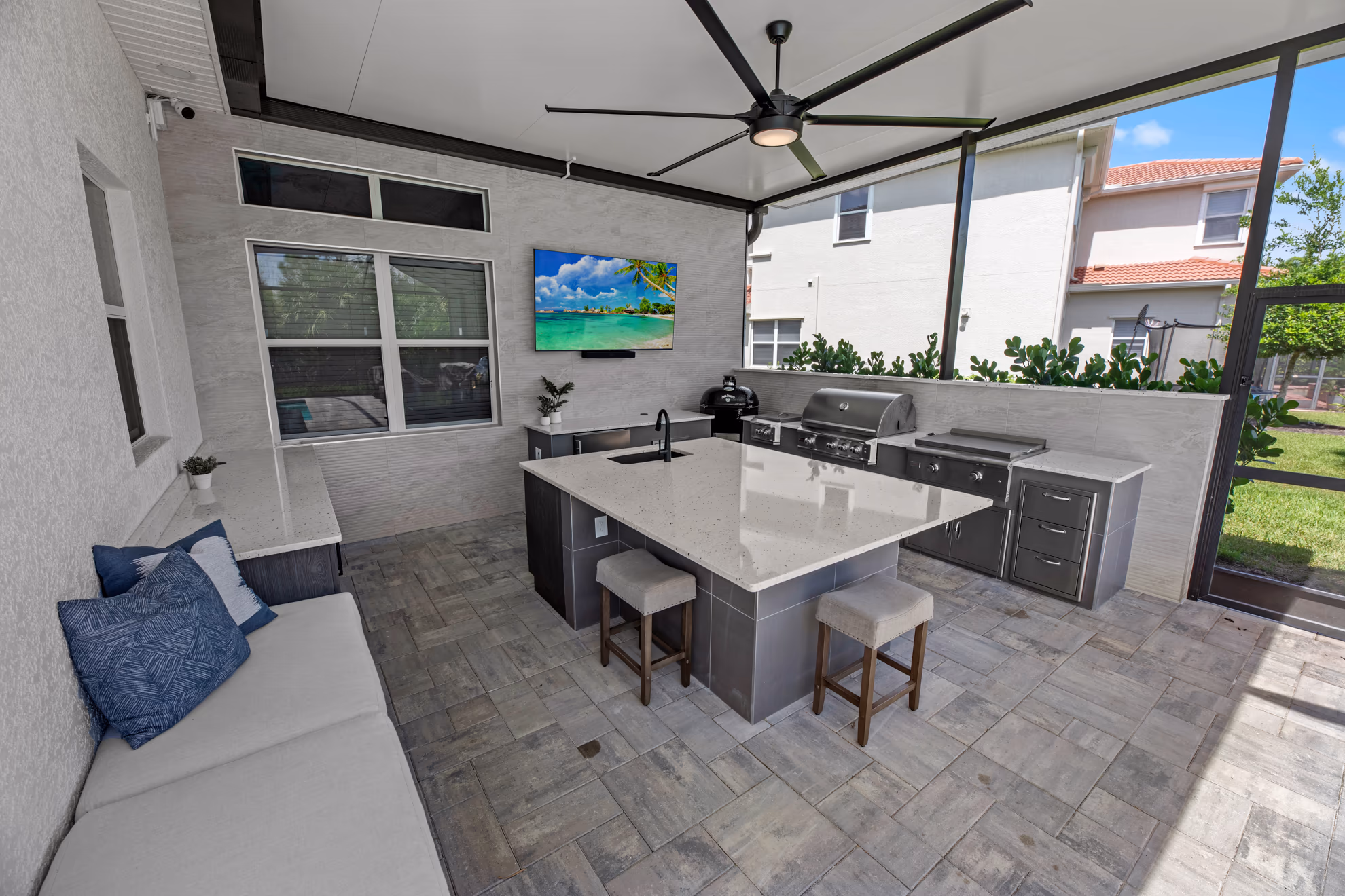Wide-angle view of the full covered lanai outdoor kitchen, from the bench to the quartz island and built-in grill