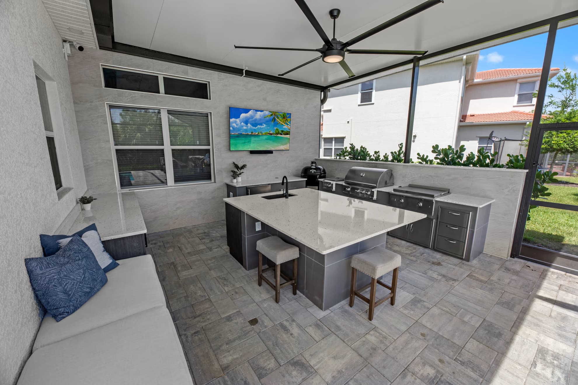 Wide-angle view of the full covered lanai outdoor kitchen, from the bench to the quartz island and built-in grill