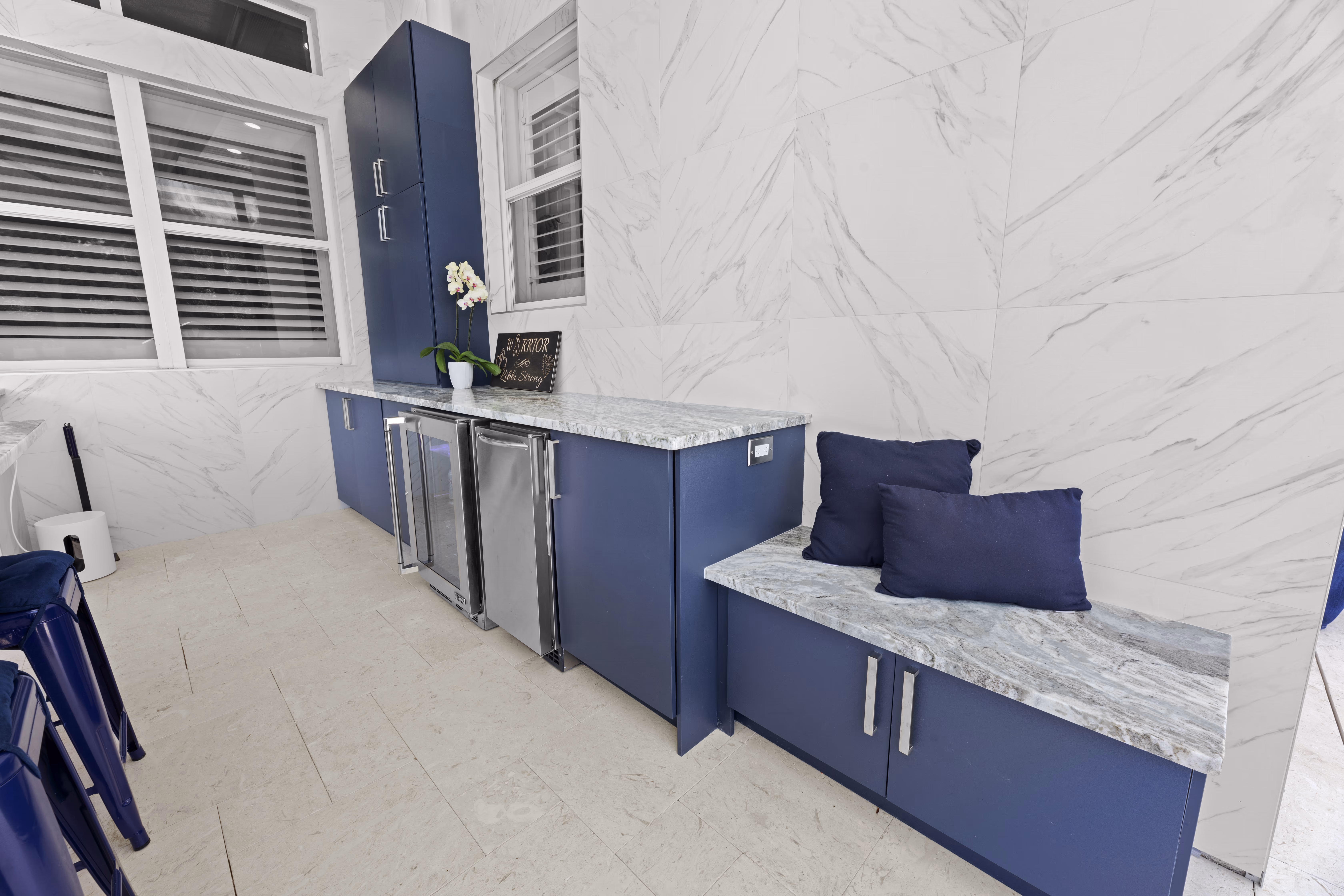 Navy cabinetry with a marble-topped bench seat and two navy pillows in the outdoor kitchen