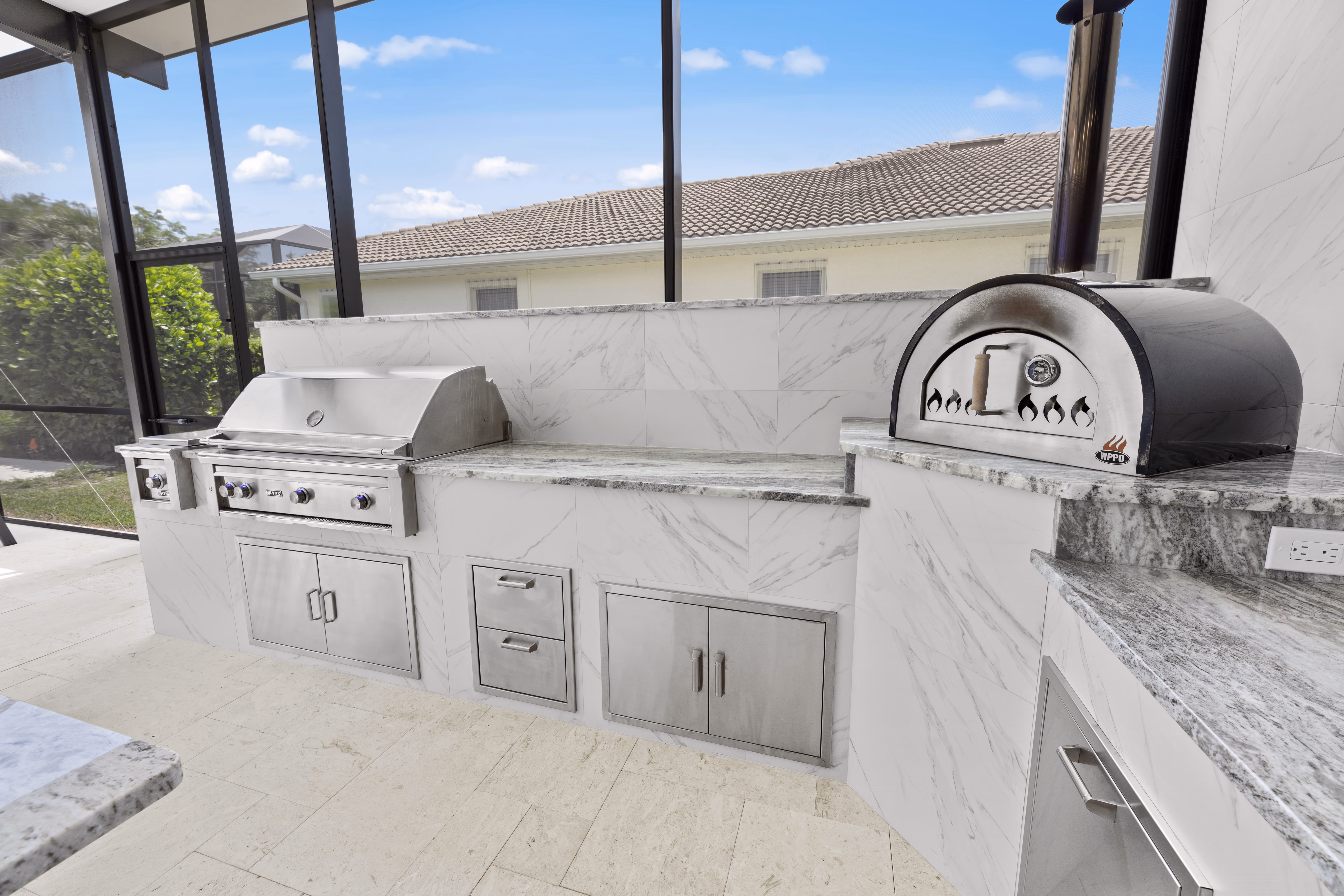Outdoor kitchen grill wall with a built-in grill, side burner, pizza oven, and stainless storage doors