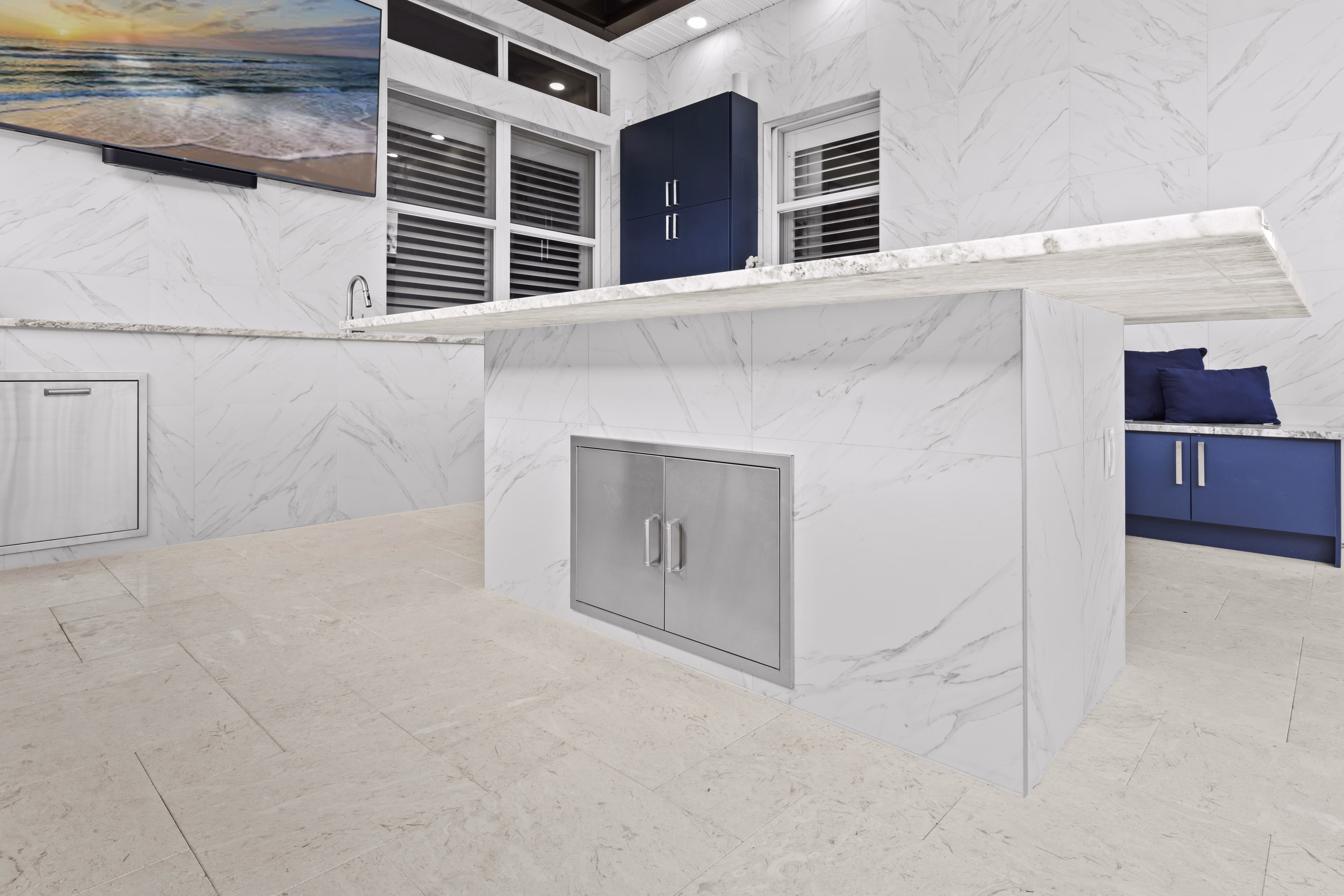 Marble-look island with a built-in stainless storage door, facing a wall-mounted TV and navy cabinetry