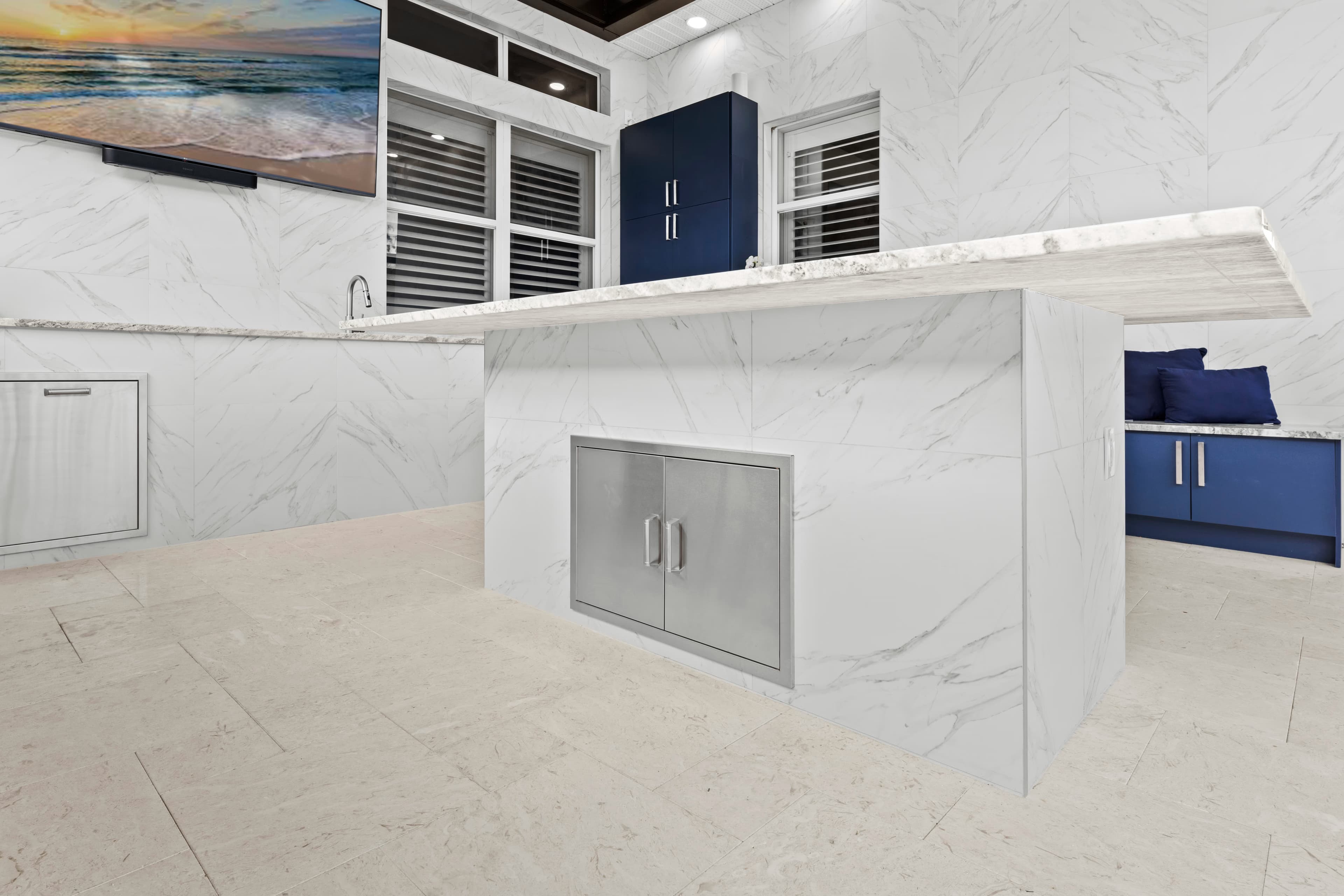 Marble-look island with a built-in stainless storage door, facing a wall-mounted TV and navy cabinetry