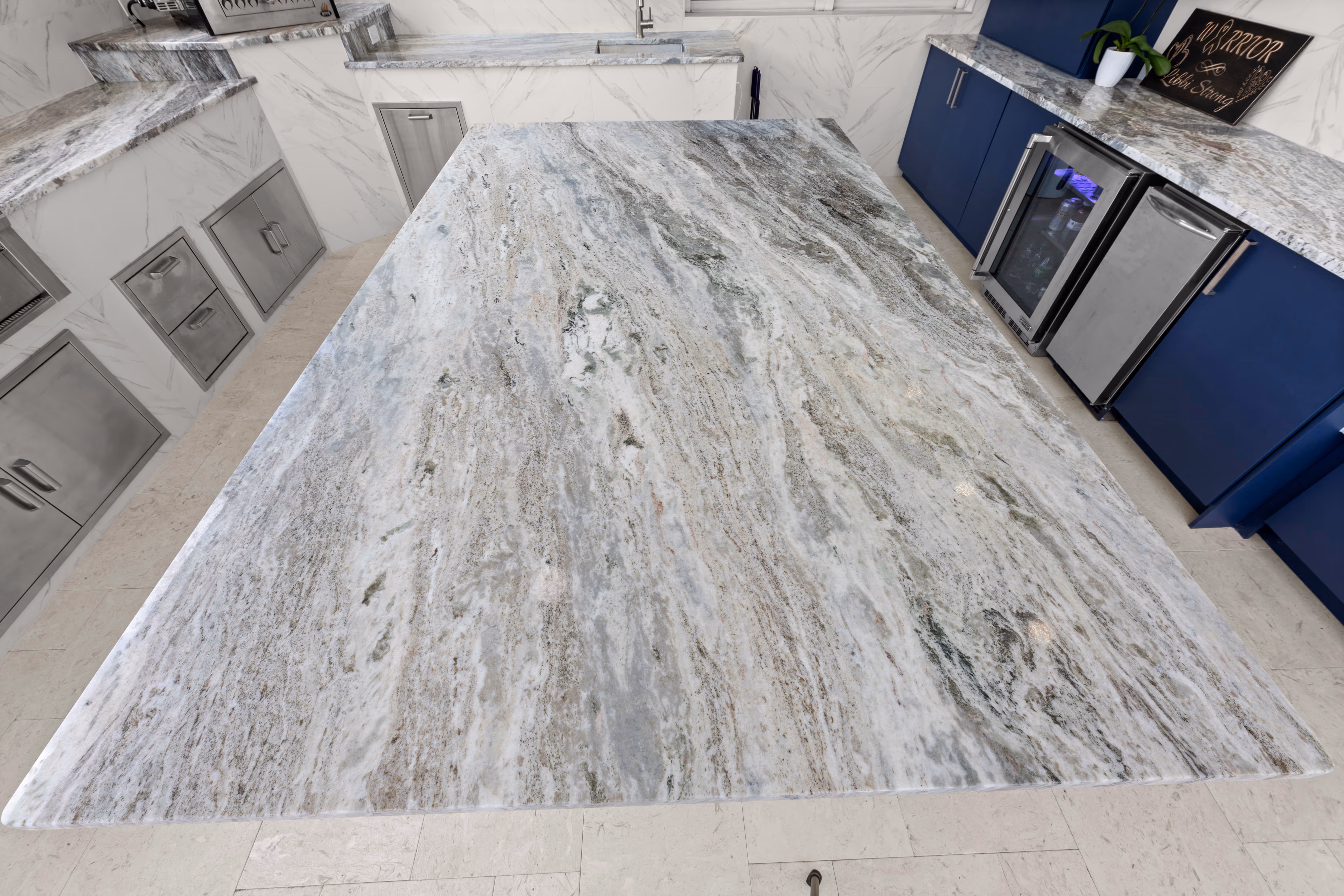 Wide view of a granite island slab from above, with navy cabinets and a wine cooler in the background